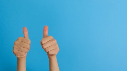 Close up of unrecognizable female makes thumb up gesture, demonstrates approval or agreement, over blue background. Body language concept. Hand sign. Like gesture