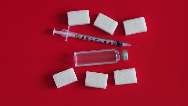 Insulin syringe with insulin lie on the cubes of refined sugar on a red background, close-up. Slow motion. The view from the top. Health care and diabetes healing concept.