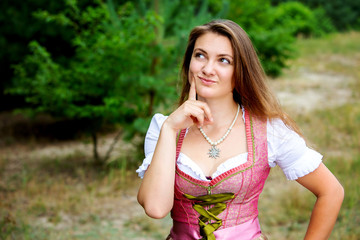Naklejka premium young woman in dirndl standing outdoors and looking thoughtfull