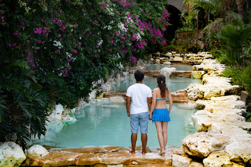 Romantic couple. Multiethnic couple at the swimming pool. View from back. Swimming pool surrounded by pink bougainvillea flowers.