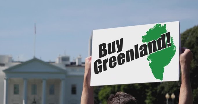 A man holds a BUY GREENLAND protest sign in front of the White House on a sunny summer day.	 	