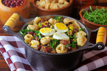Feijao Tropeiro typical dish of Brazilian cuisine, made with beans, bacon, sausage, collard greens, eggs, on rustic wooden table.