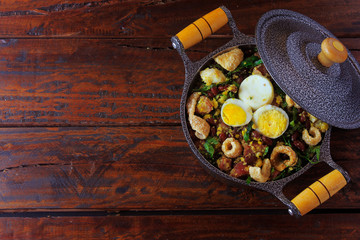 Feijao Tropeiro typical dish of Brazilian cuisine, made with beans, bacon, sausage, collard greens, eggs, on rustic wooden table.