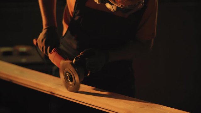 Woodworker using grinding tool for polishing plank. Craftman working in beautiful sunset light. Woodworking, carpentering, craft, profession concept