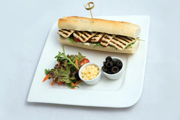 A high contrast Hero shot of a Grilled Halloumi cheese baguette with olives & salad on the side, on a minimal white background with a 75 degree angle from slant zoomed perspective
