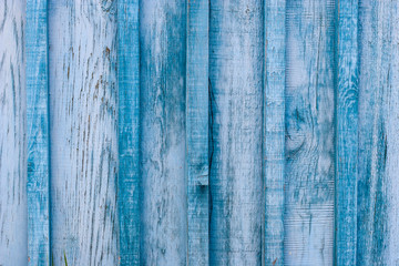 Fototapeta na wymiar Grunge background. Wooden old blue fence. The gaps between the boards are clogged with slats. The paint is peeling and cracked.