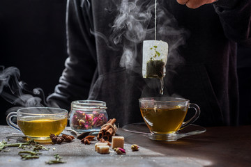 The steam from man with jecket Jean is soaking tea bag on vintage white cup, preparing hot tea.Dipping teabag on cup,hot food and healthy meal concept