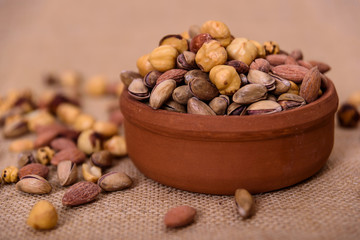 Almonds, pistachios, hazelnuts and round nuts in bowl on textured light brown background. Table view food.