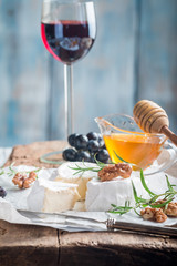 Brie cheese and a slice on a wooden board with nuts, honey and rosemary.