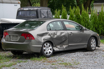 Gray car in a junk yard with damage to the rear panel, door and tire of a gray car due to an...