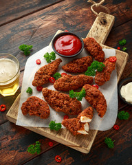 Breaded chicken strips with beer, ketchup and mayonnaise on wooden board