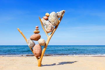 Multicolored balanced stones on an wooden snags, on a blue sky and sea background