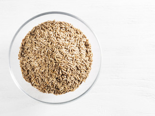 Cumin seeds (Cuminum), Jeera in a glass cup on a white wooden background with copy space
