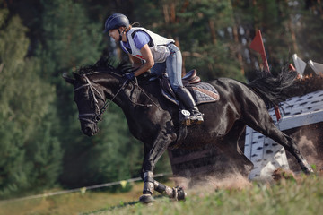 portrait of woman rider and black sport horse galloping energetically during eventing competition