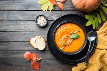 Pumpkin soup in a black plate on dark wooden background. Autumn decorations. Top view