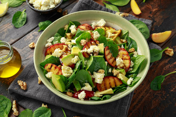 Summer Peach Salad with spinach, avocado, walnuts and feta cheese in rustic bowl. healthy food.