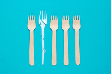 Minimalistic ecologically clean still life. Pop Art. Broken plastic fork among many wooden forks on blue background. Cutlery made from natural materials