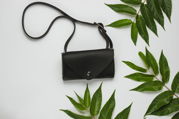 Leather waist bag on white background with green tropical leaves. Top view