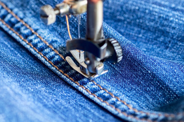 On an outdated sewing machine with a mechanical manual drive, men's pants are made of a dense blue...