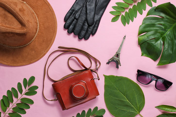 Jorney to Paris. Women's accessories, retro camera, figurine of the Eiffel tower on pink pastel background with green leaves. Top view