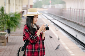 Fototapeta na wymiar Young beautiful female travel photographer enjoys taking photo during her trip at railway station. Asian woman travel with camera having fun making pictures while waiting for train.
