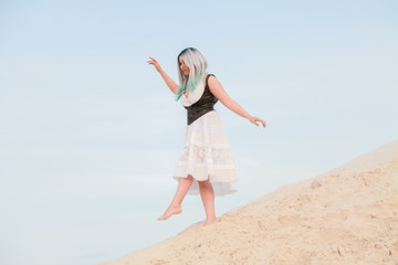 Young beautiful Caucasian woman in white dress and brown leather waistcoat posing in desert landscape with sand.