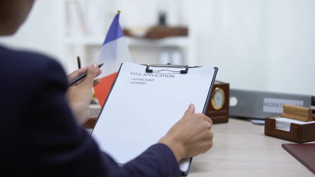 Embassy employee approving visa application, french flag on table, migration law