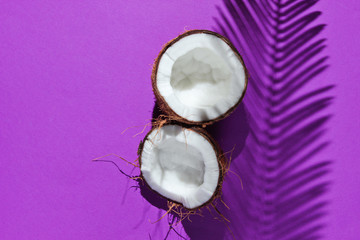 Minimalistic tropical still life. Two halves of chopped coconut with shadows from palm leaves on purple background. Creative fashion concept. Top view.