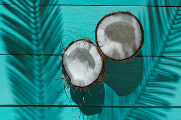 Minimalistic tropical still life. Two halves of chopped coconut with shadows from palm leaves on blue wooden background. Creative fashion concept. Top view.