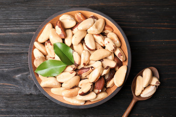 Bowl and spoon with Brazil nuts on wooden background, top view
