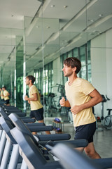 Young sports man running on a treadmill at gym doing workout