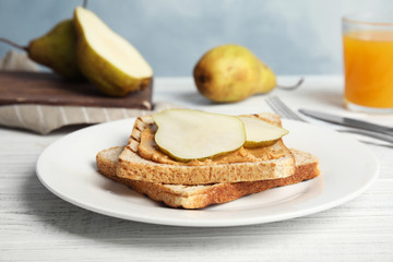 Slice of bread with peanut butter and pear on white wooden table