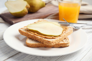 Slice of bread with peanut butter and pear on white wooden table