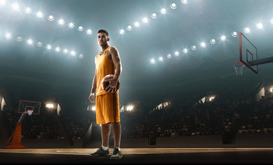 Basketball player in sports uniform on empty floodlit basketball court with the ball