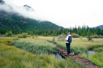 Woman With Backpack Hiking Into The Forest Mountains.