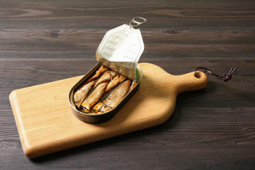 Board with tin can of sprats on wooden table