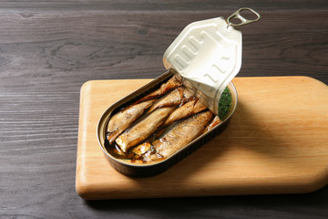 Board with tin can of sprats on wooden table