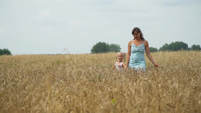 Little Girl with Mother Walking Through the Golden Wheat Field in Autumn Day. Slow Motion. Freedom and Enjoying Nature Concept