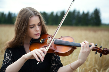 close-up portrait of a young woman with her eyes down and playing the violin on a wheat field. © Denis Ivanov