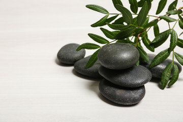Spa stones and green leaves on white table, space for text