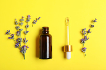 Bottle of essential oil and lavender flowers on yellow background, flat lay