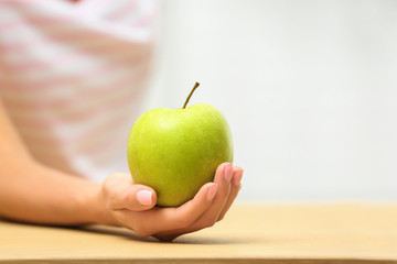 Woman holding fresh green apple at table, closeup. Space for text