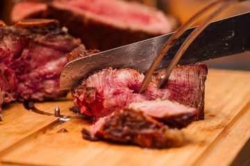 Slicing rare beef steak on a woodeng cutting board, close-up.