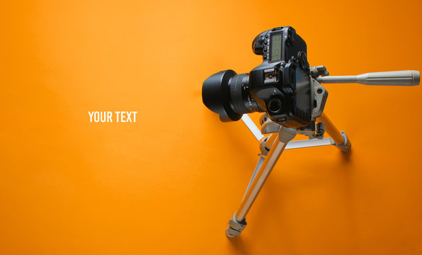 Modern digital camera with tripod on orange background. Minimalism. Copy space. Top view