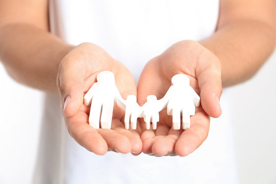 Young man holding wooden family figure on white background, closeup of hands