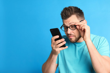 Man with vision problems using smartphone on blue background, space for text