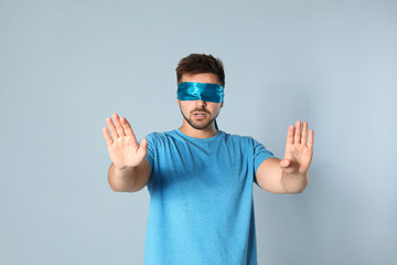 Naklejka premium Young man with light blue blindfold on grey background