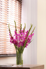 Vase with beautiful pink gladiolus flowers on wooden table in room, space for text