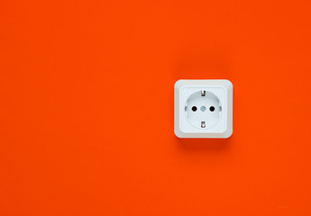 White plastic power socket on orange background. Wall with copy space. Minimalism
