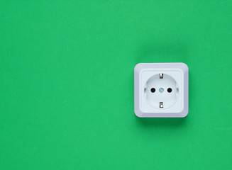 White plastic power socket on green background. Wall with copy space. Minimalism